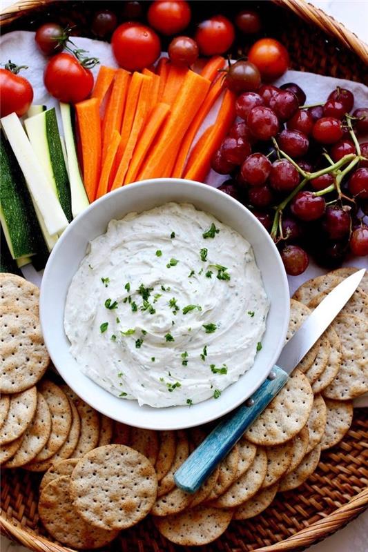 sur kräm och gräslök, inuti en vit skål, vegetariska aptitretare fingermat, kex och grönsaker på sidan