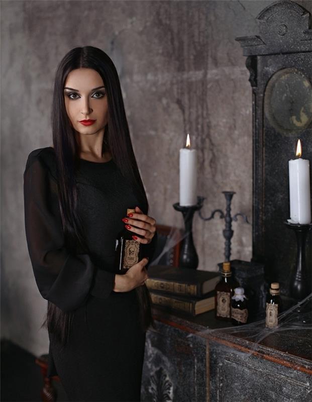 فكرة الزي Morticia Addams ، فستان أسود بأكمام شفافة ، كتب grimoire ، قوارير شموع على الخلفية ، شعر طويل ناعم الظل شاحب