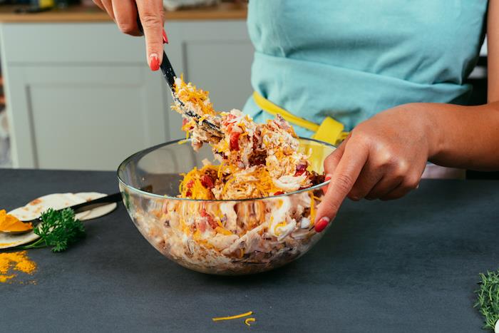 kvinna med rött nagellack, håller en glasskål, blandar ingredienser, med en svart spatel, tacoköttrecept