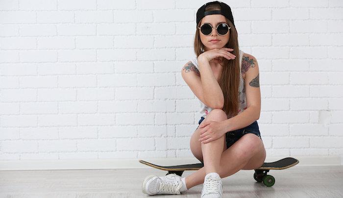 Krásne hipsterské dievča so skateboardom na svetlom pozadí