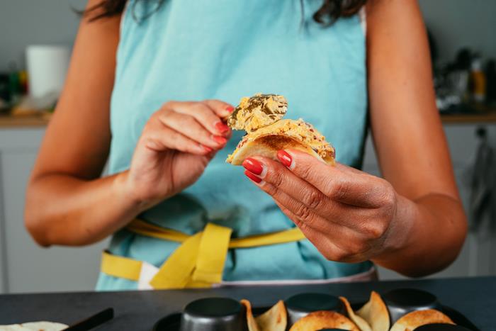 kvinna med rött nagellack, fyllning av tortillainpackningar, recept på tacokött, mässingssked, blått förkläde